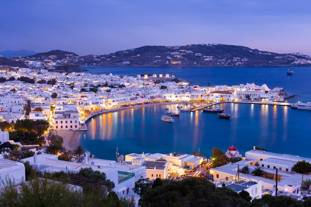Marina in Greece after sunset with lights reflecting off the water.