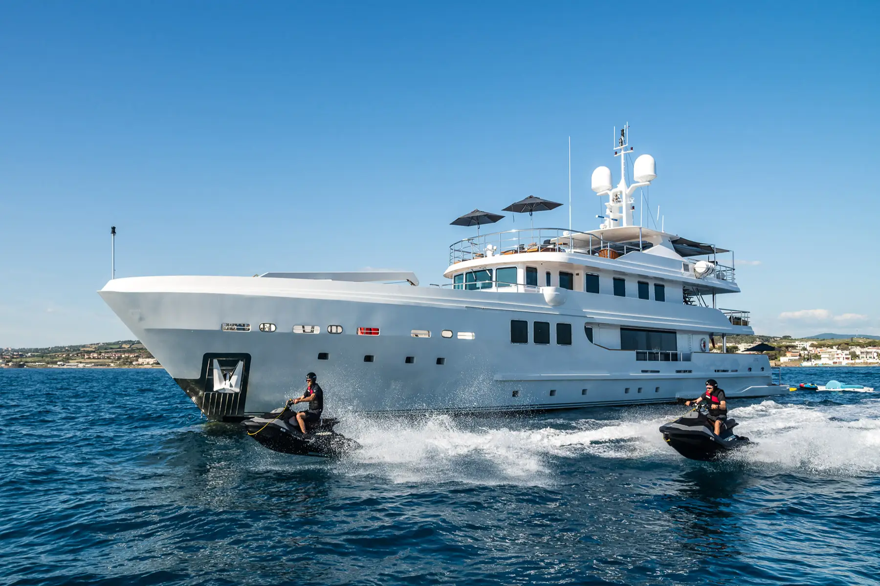 The yacht R23 cruising through the water with jet skis beside it.