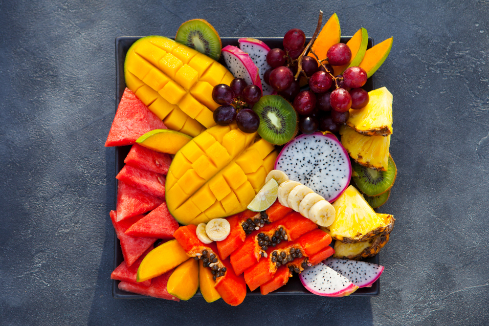 Mango, watermelon. dragonfruit, papaya, kiwis, and other exotic fruits all on a black plate.
