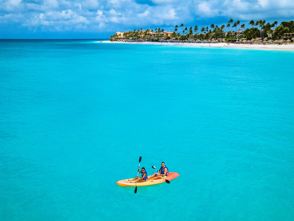 Bright blue ocean with the beach in the distance and two people sitting in a yellow kayak.