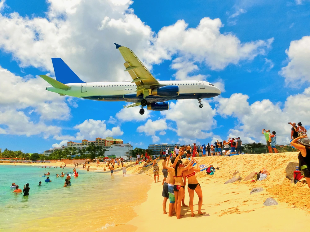 Maho Beach on St Martin with a jumbo jet flying low over a crowd of cheering people.