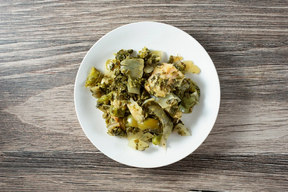 A while dish filled with Callaloo and salt fish on a wooden table.