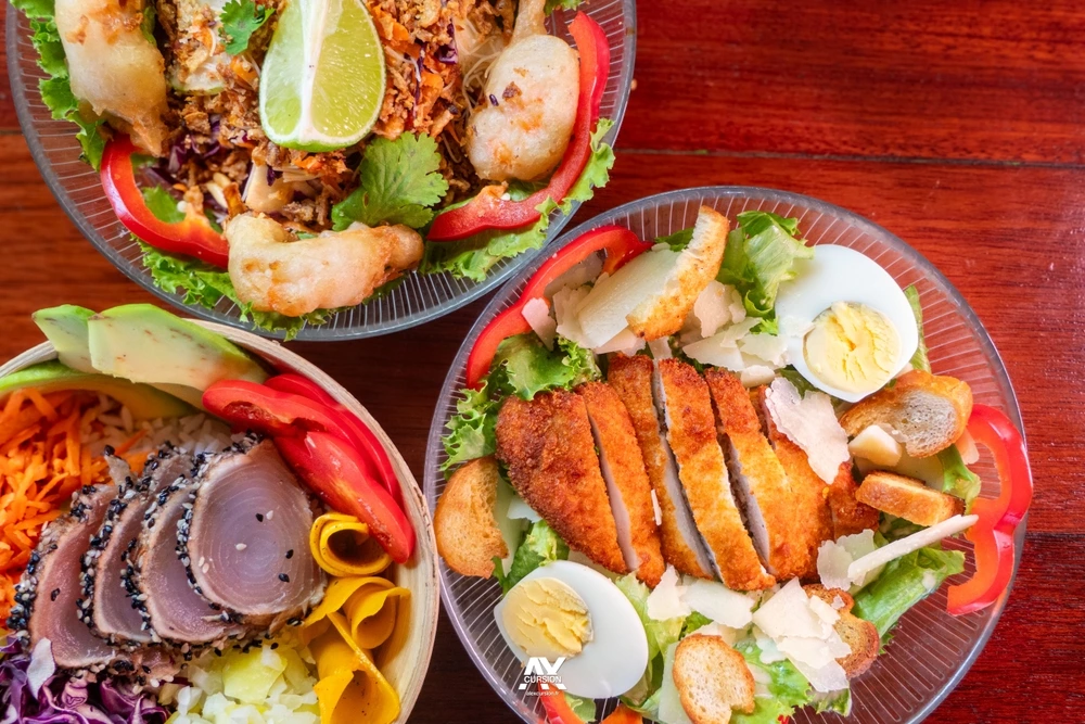 An array of colourful Caribbean food in glass dishes on a wooden table.