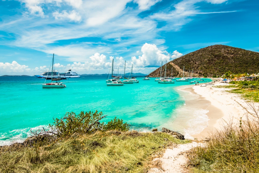 Bright blue waters and white sand beaches of Jost Van Dyke with multiple yachts on the water.