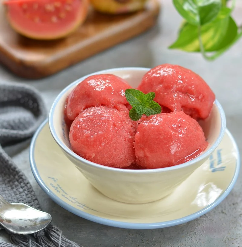 Four scoops of guava sorbet in a white porcelain bowl on a white saucer.