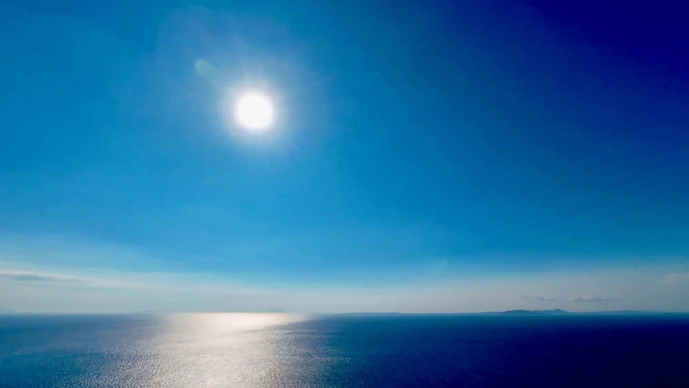 The sun shining brightly over deep blue water.