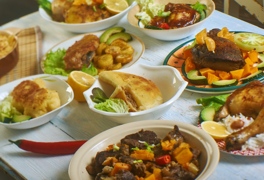 A vast selection of different Caribbean foods on different sized dishes and plates free for people to pick and choose from.