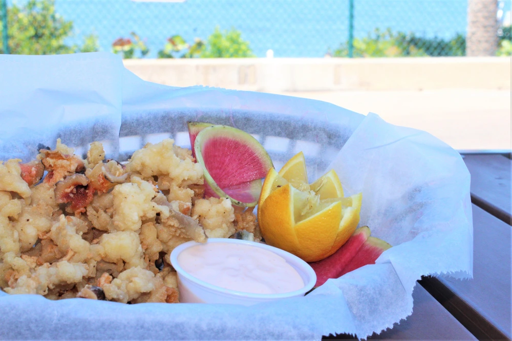 A small basket with white paper and filled with cracked island conch, lemon and sauce.