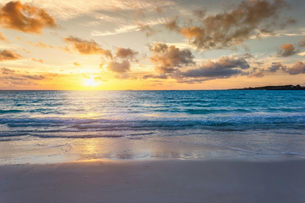 The sun setting over bright blue waters. Some clouds are moving past in the sky.