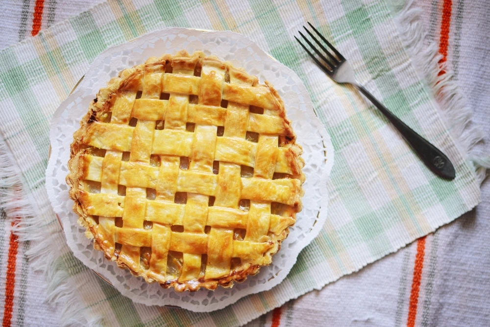 A pineapple tart on a white plate with a fork beside it.