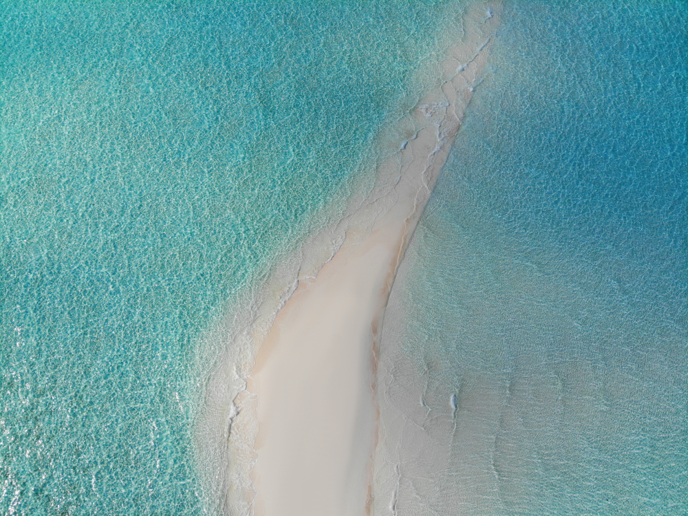 A thin sandbar surrounded by bright blue water.