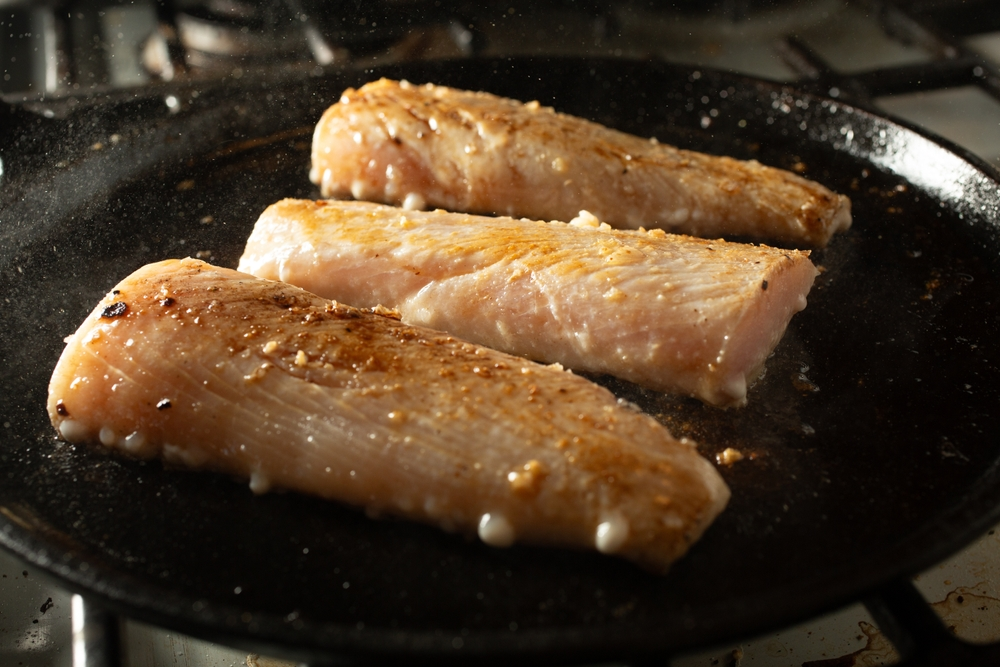 Three Mahi Mahi fillets being seared on a black pan.