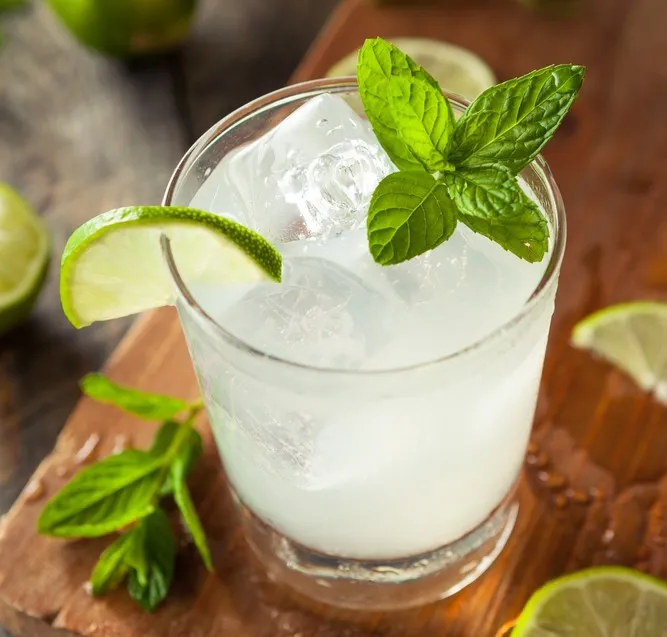 Switcha, a Bahamian limeade in a glass with ice and mint. A lime wedge is on the rim of the glass.
