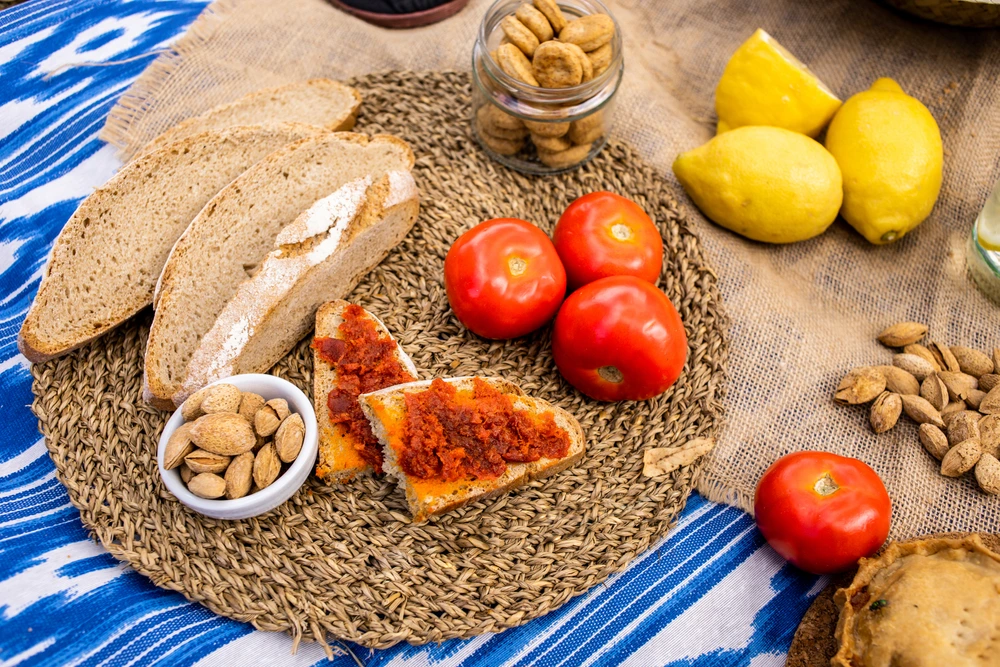 Traditional Balearic food on a woven mat, including bread, spreads, tomatos, lemons and nuts.