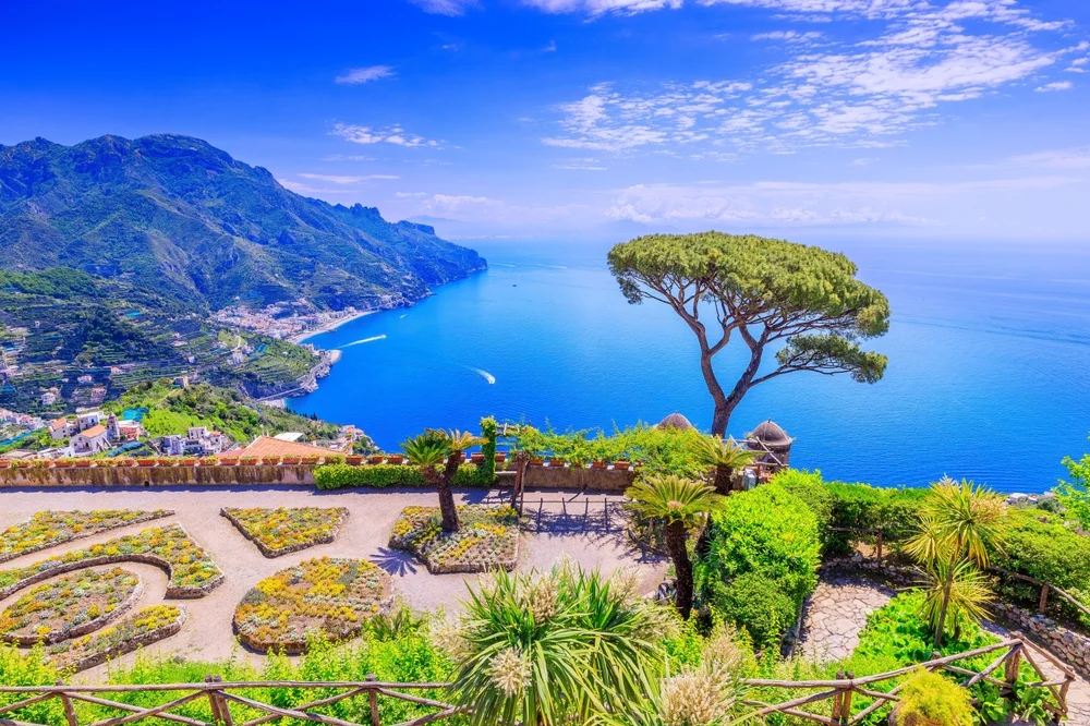 The Amalfi Coast with clear blue skies and deep blue water beside green hills and a balcony overlooking them.