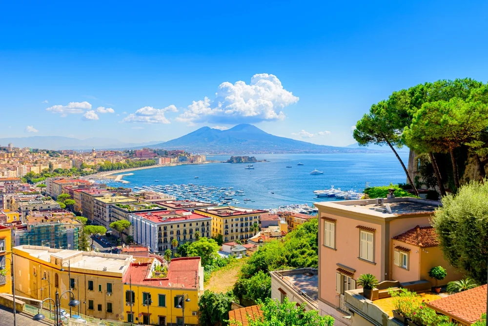The city of Naples besides the bay with views of Mount Vesuvius and yachts and boats in the bay.